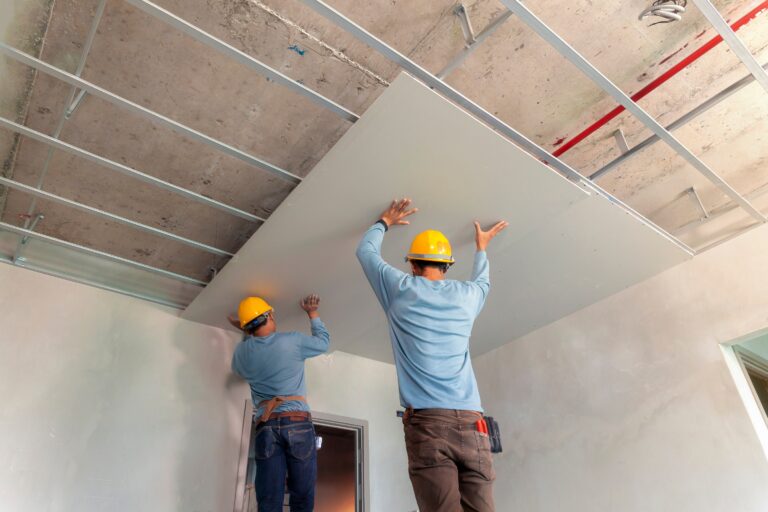 Zwei Bauarbeiter montieren Gipskartonplatten an der Decke – Trockenbauarbeiten im Innenausbau.