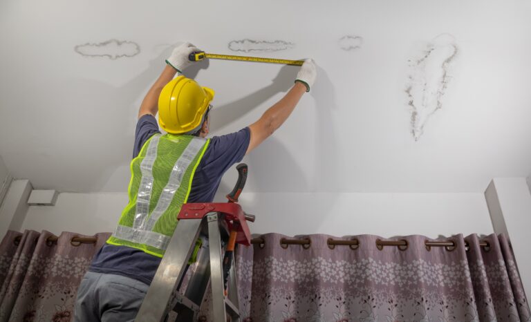Handwerker misst feuchte Stelle an Zimmerdecke – Wasserschaden und Renovierungsarbeiten.