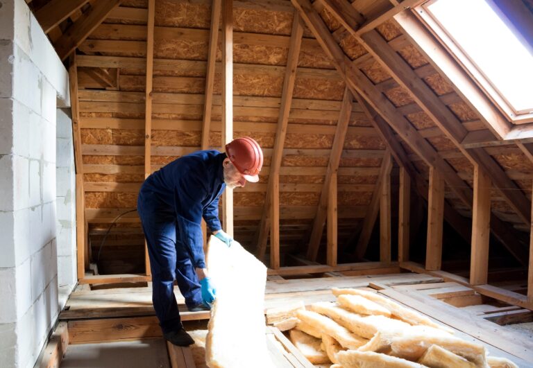 Bauarbeiter verlegt Dämmmaterial im Dachboden – energetische Dachisolierung.