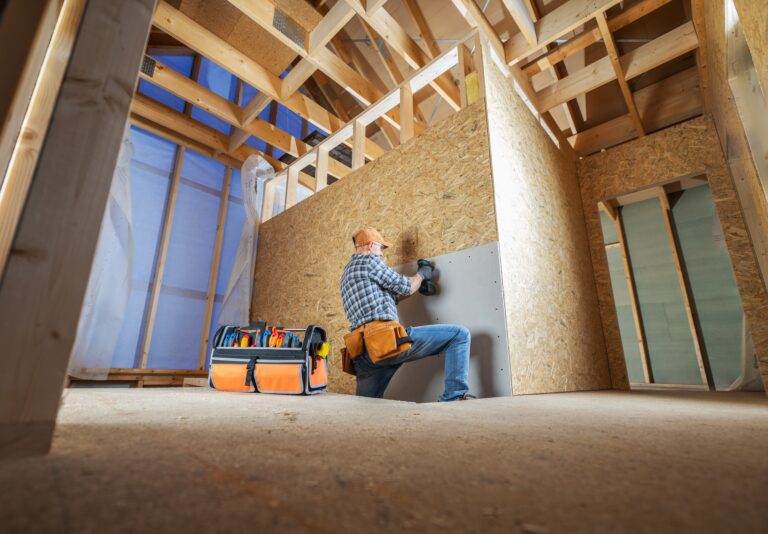 Handwerker beim Innenausbau eines Holzhauses montiert Trockenbauplatten und Deckensysteme – Bauarbeiten mit Werkzeugkoffer im Rohbau.